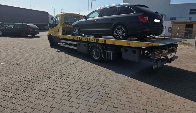 Kombi bez widocznych uszkodzeń przewożone na lawecie pomocy drogowej Tuszyn przez parking przy hali magazynowej