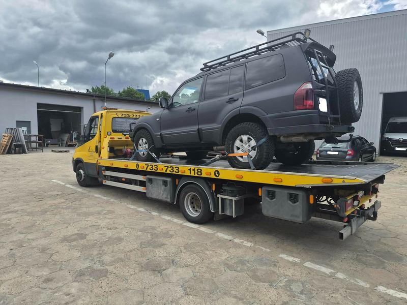 Terenowy SUV z bagażnikiem dachowym stoi na lawecie na firmowym placu, autoholowanie Tuszyn