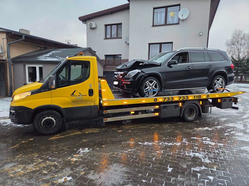 Laweta pomocy drogowej Tuszyn transportuje rozbity SUV z uszkodzonym przodem na zaśnieżonej posesji