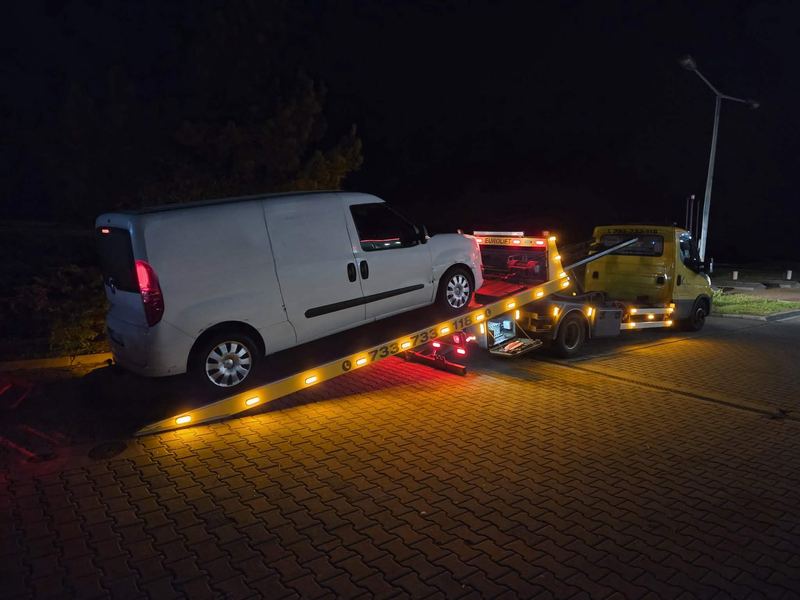 Nocny transport auta dostawczego lawetą pomocy drogowej Tuszyn na oświetlonym parkingu