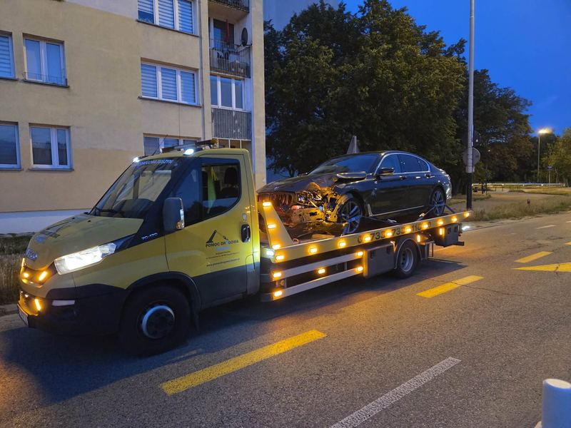 Nocą laweta pomocy drogowej Tuszyn zabiera rozbity w wypadku samochód osobowy ulicą przy bloku