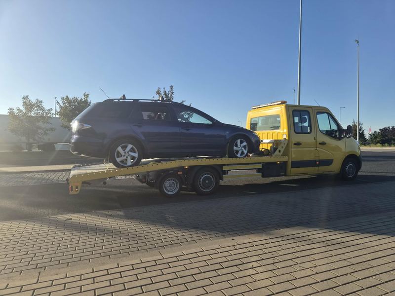 Dwukabinowa laweta pomocy drogowej Tuszyn z załadowanym autem kombi na parkingu o zachodzie słońca