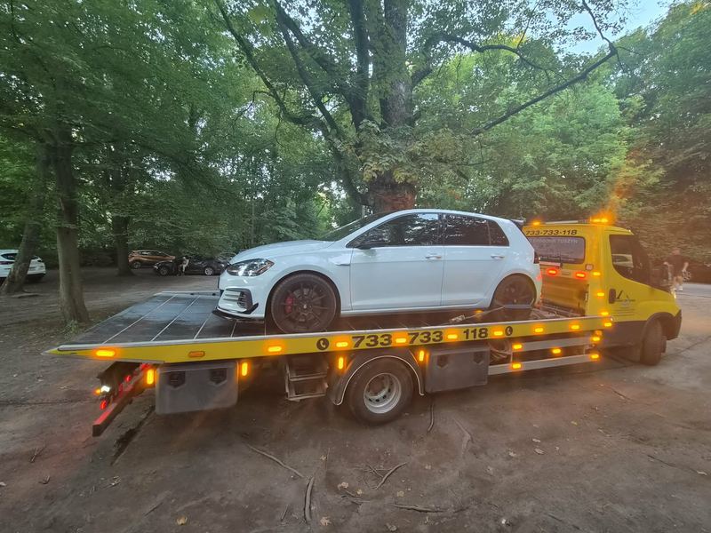 Transport sportowego hatchbacka lawetą pomocy drogowej Tuszyn na zacienionym leśnym parkingu