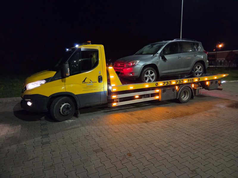Nocą laweta pomocy drogowej Tuszyn dowozi SUV-a na oświetlony miejski parking