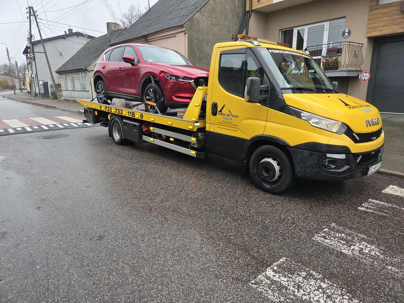 Laweta pomocy drogowej Tuszyn transportuje uszkodzonego w kolizji SUV-a ulicą osiedlową w deszczowy dzień