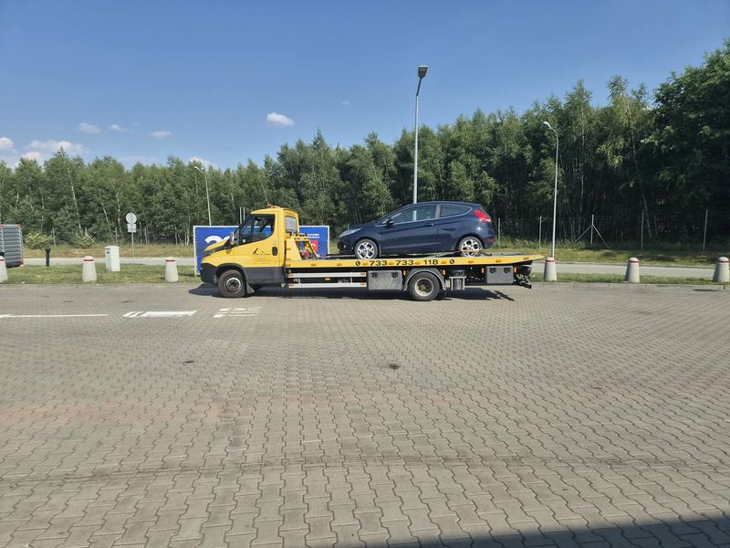 Laweta pomocy drogowej Tuszyn przewozi osobowego hatchbacka przez pusty miejski parking