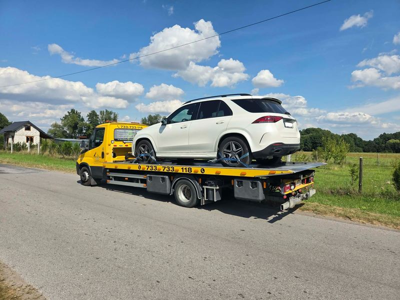 Sprawny SUV jedzie na lawecie wiejską drogą po awarii, na miejscu pomoc drogowa Tuszyn