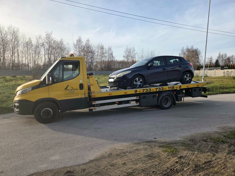 Laweta wiezie kompaktowego hatchbacka pustą drogą wśród bezlistnych drzew, pomoc drogowa Tuszyn