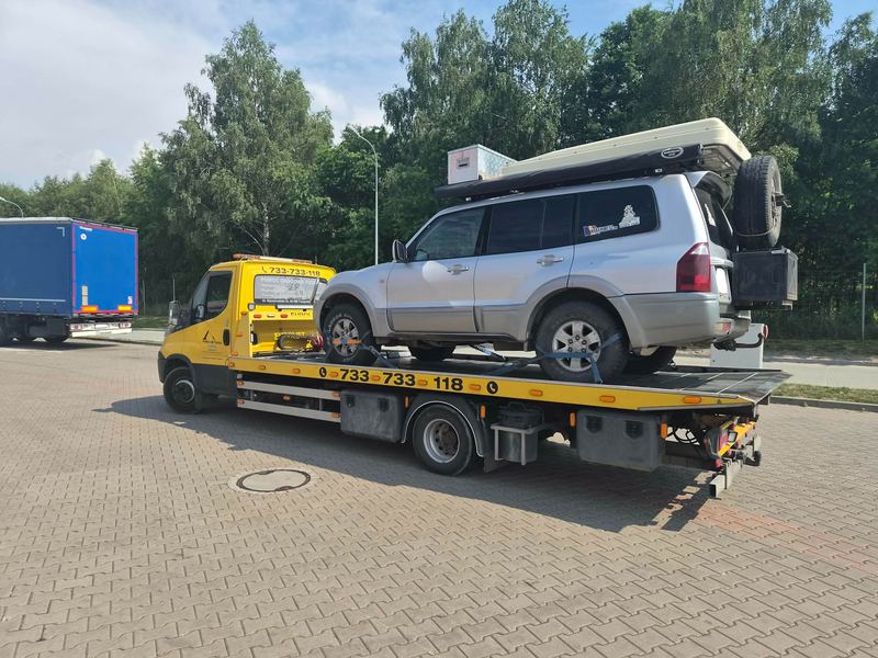 Terenowy SUV z namiotem dachowym i zapasowym kołem stoi na lawecie na słonecznym parkingu