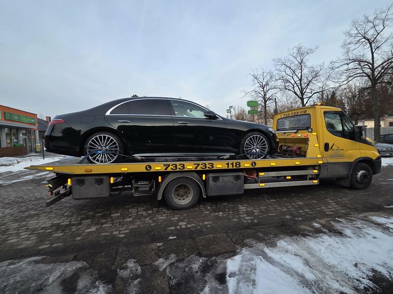 Laweta pomocy drogowej Tuszyn przewozi elegancki sedan klasy premium ulicą miasta obok zaśnieżonego pobocza
