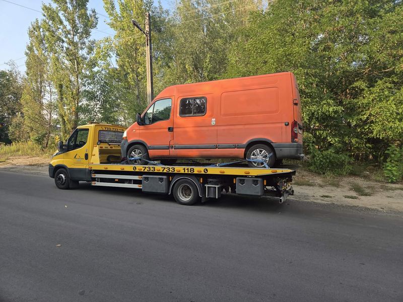 Laweta z pomocy drogowej Tuszyn wiezie sprawny bus dostawczy wiejską drogą wśród drzew