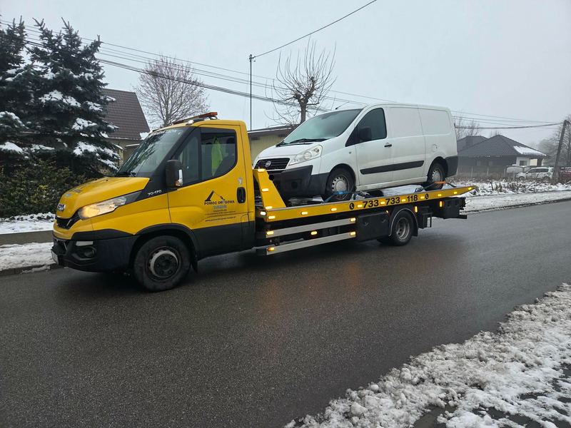 Laweta pomocy drogowej Tuszyn wiezie bus dostawczy ośnieżoną ulicą zimą w małej miejscowości