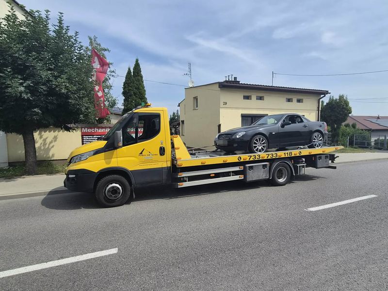 Laweta pomocy drogowej Tuszyn przewozi nieuszkodzone coupe ulicą osiedlową w słoneczny dzień