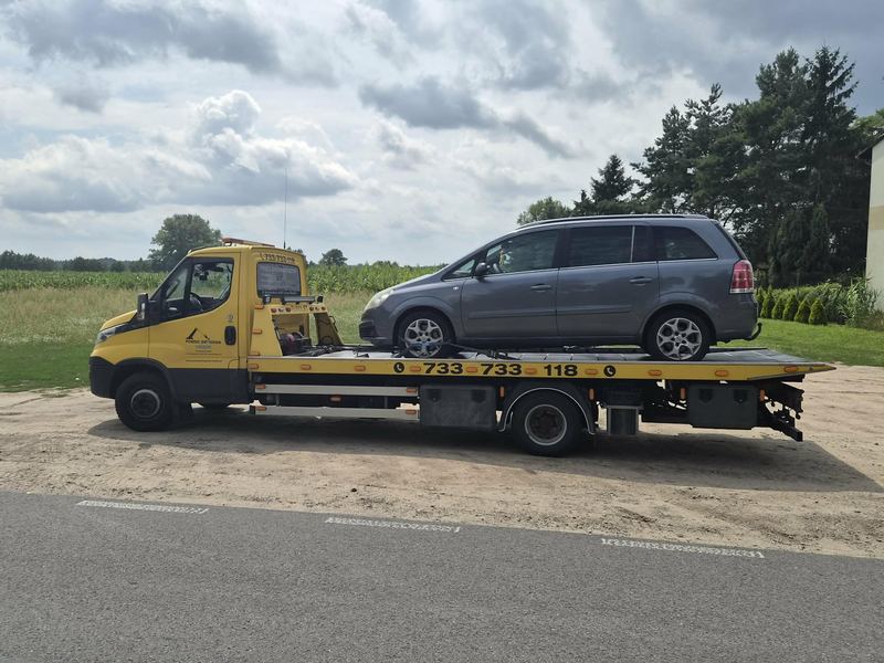 Minivan jest przewożony lawetą pomocy drogowej Tuszyn polną drogą wśród pól