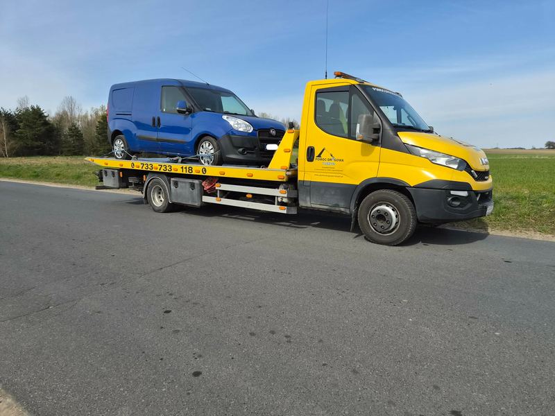 Laweta pomocy drogowej Tuszyn wiezie niewielkie auto dostawcze drogą wśród pól w słoneczny dzień