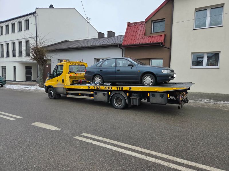 Wysłużony sedan przewożony na lawecie zimową ulicą w mieście, pomoc drogowa Tuszyn