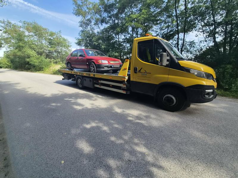 Starszy hatchback przewożony na lawecie wąską drogą wśród drzew w słoneczny dzień, pomoc drogowa Tuszyn