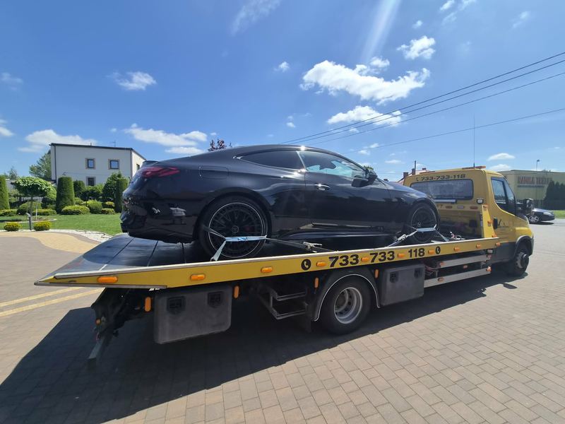Eleganckie coupé jedzie na lawecie pomocy drogowej Tuszyn po kostce brukowej przed posesją