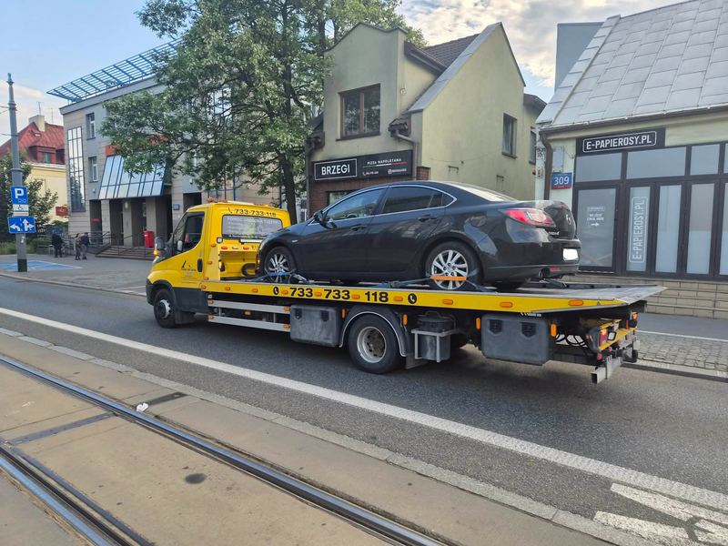 Sedan przewożony na lawecie ulicą w centrum miasta obok torów tramwajowych, pomoc drogowa Tuszyn