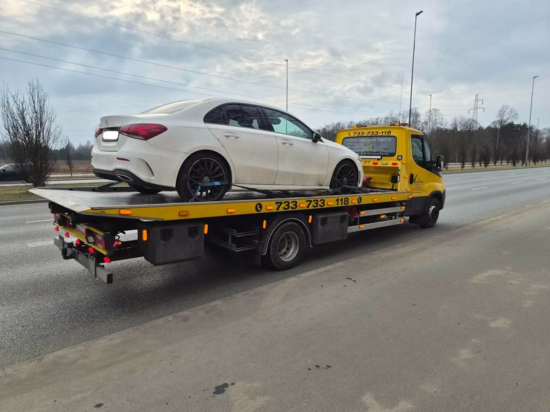 Laweta wiezie sprawny sedan szeroką drogą ekspresową w ramach usługi pomocy drogowej Tuszyn