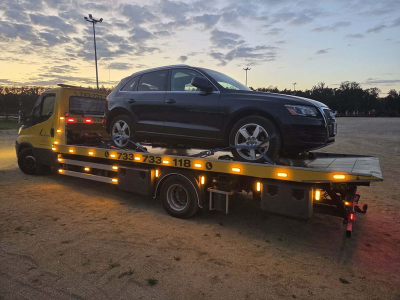 Laweta transportuje sprawny SUV przez piaszczysty plac o zmierzchu, pomoc drogowa Tuszyn