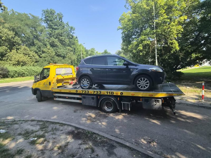 Laweta pomocy drogowej Tuszyn wiezie sprawny SUV spokojną ulicą w słoneczny dzień