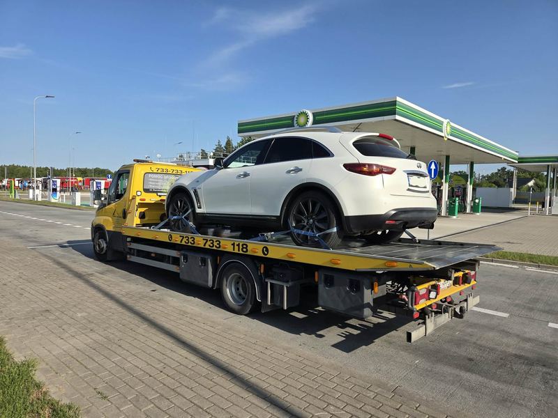 Laweta pomocy drogowej Tuszyn z SUV-em na platformie na stacji paliw przy trasie