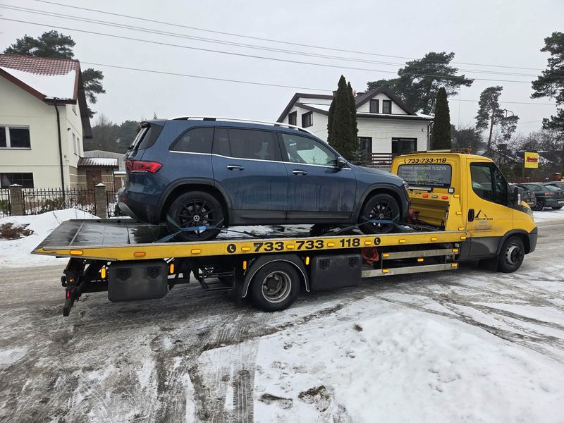 Laweta pomocy drogowej Tuszyn transportuje sprawny SUV zaśnieżoną ulicą osiedla domków jednorodzinnych