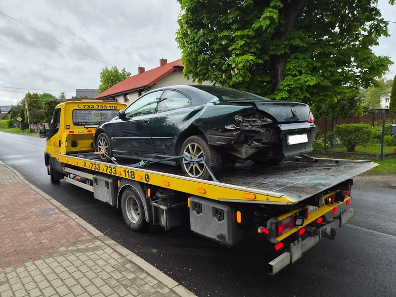 Uszkodzony z tyłu samochód osobowy przewożony lawetą ulicą w mieście podczas pochmurnego dnia