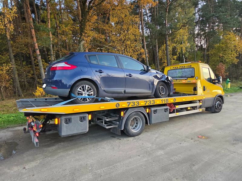 Laweta pomocy drogowej Tuszyn wiezie hatchback z rozbitym przodem leśną drogą jesienią
