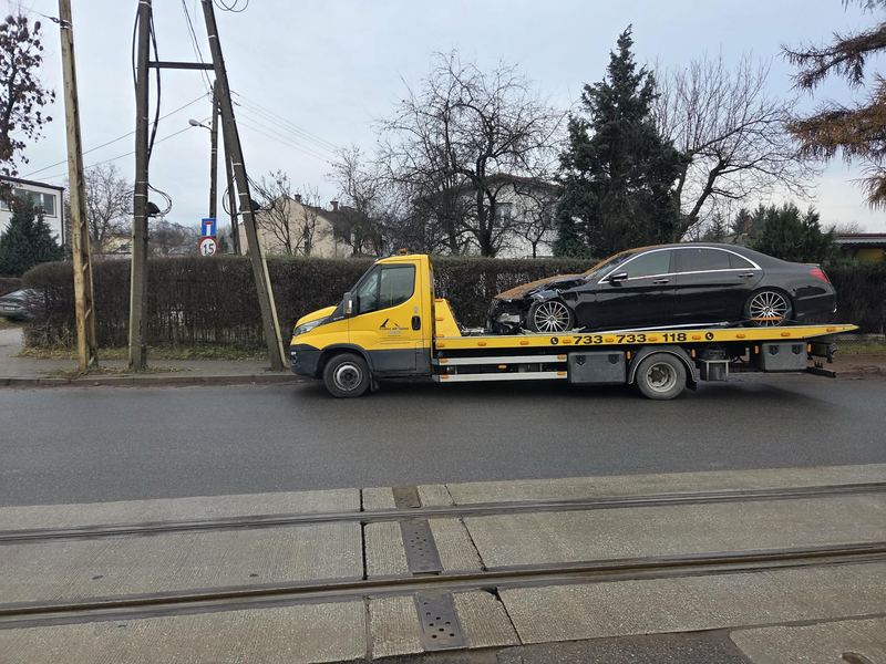 Rozbity samochód osobowy na lawecie pomocy drogowej Tuszyn, holowany ulicą miasta z torami tramwajowymi