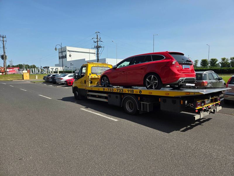 Laweta pomocy drogowej Tuszyn wiezie sprawne kombi Volvo V60 ulicą w mieście w słoneczny dzień