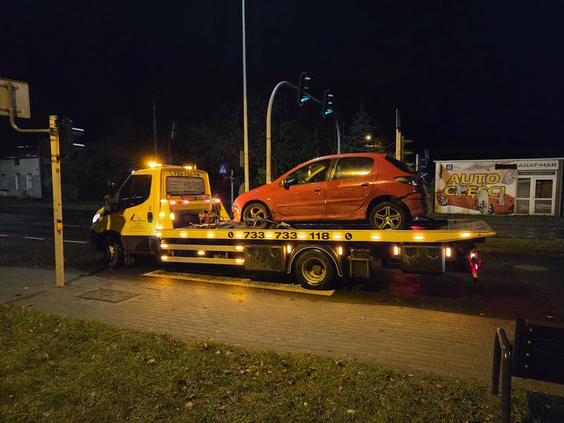 Holowanie nocą małego uszkodzonego auta osobowego lawetą pomocy drogowej Tuszyn przy skrzyżowaniu z sygnalizacją