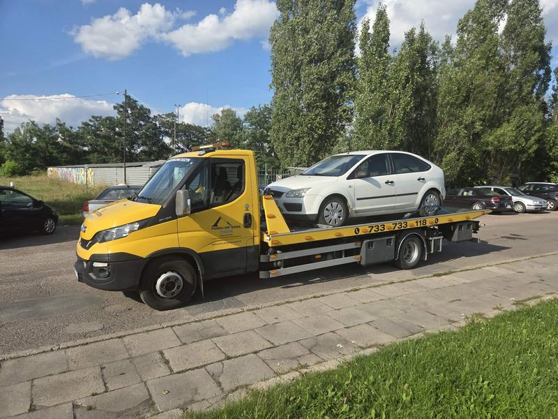 Nieuszkodzony hatchback stoi na platformie lawety pomocy drogowej Tuszyn wśród zaparkowanych samochodów