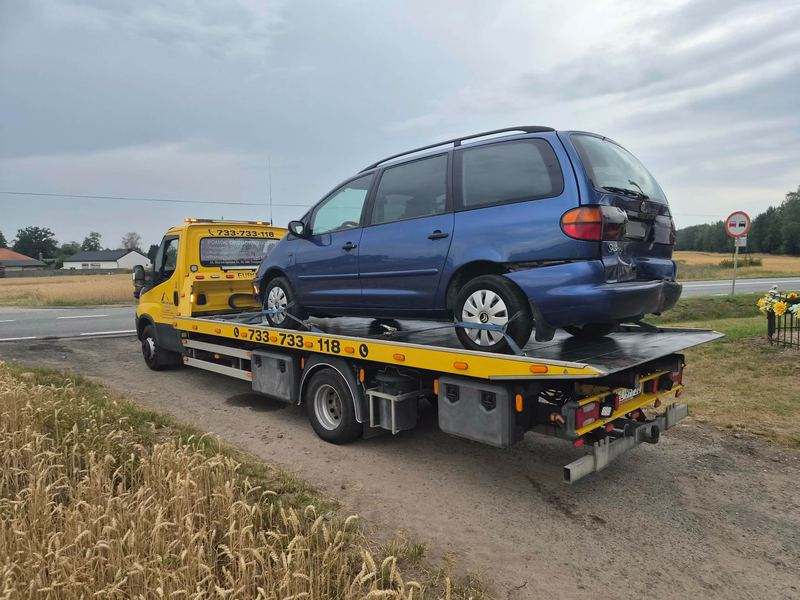 Uszkodzony z tyłu minivan na lawecie pomocy drogowej Tuszyn na wiejskiej drodze o zmierzchu