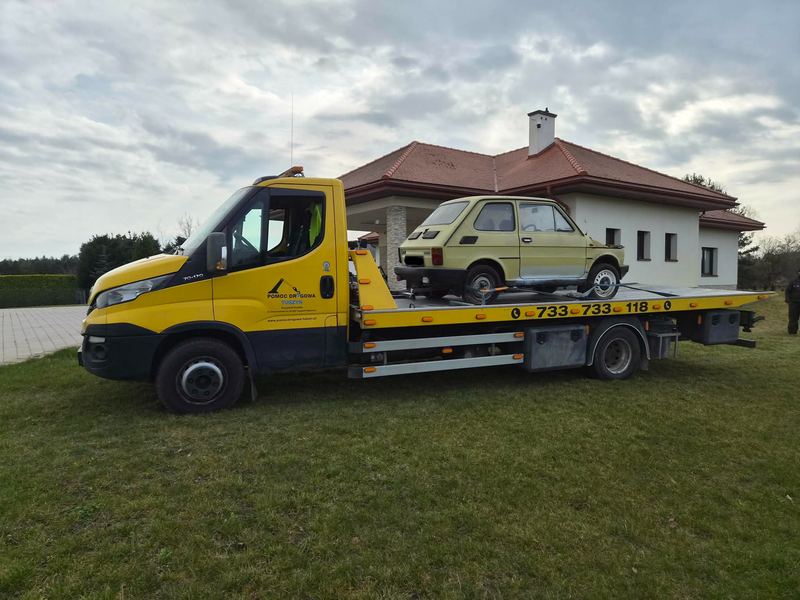Holowanie zabytkowego małego auta lawetą pomocy drogowej Tuszyn na trawniku przed domem