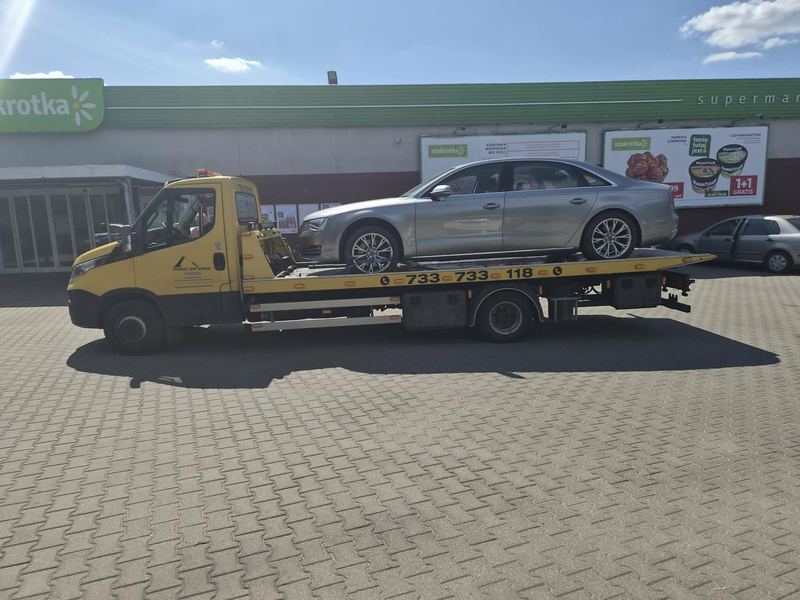 Pomoc drogowa Tuszyn lawetą transportuje sprawny sedan spod supermarketu w słoneczny dzień