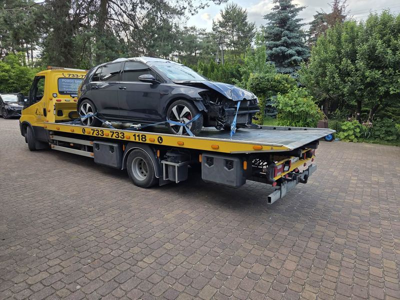 Rozbity z przodu hatchback owinięty folią stoi na lawecie pomocy drogowej Tuszyn na posesji wśród zieleni