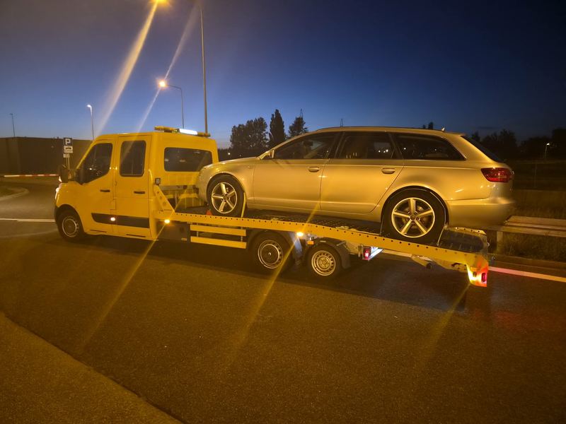 Kombi transportowane nocą lawetą pomocy drogowej Tuszyn na oświetlonym parkingu przy drodze
