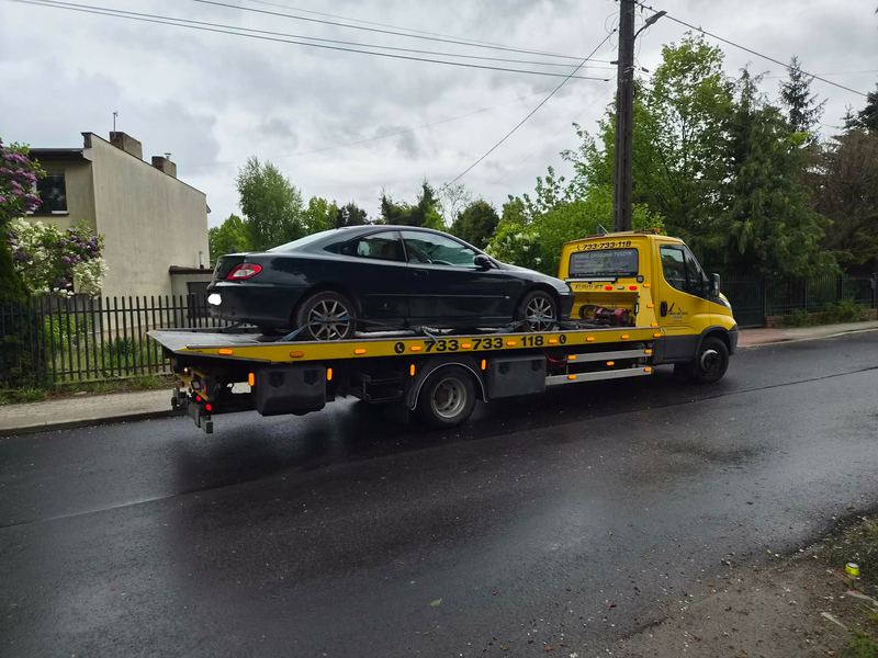 Sportowe coupe stoi na lawecie pomocy drogowej Tuszyn na mokrej ulicy osiedlowej po deszczu