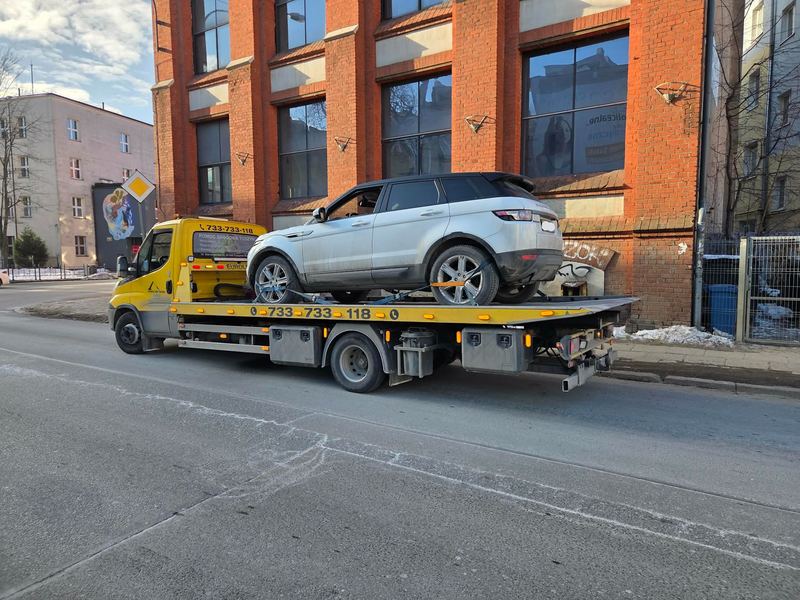 SUV na lawecie pomocy drogowej Tuszyn jedzie zimą ulicą miasta obok ceglanej kamienicy