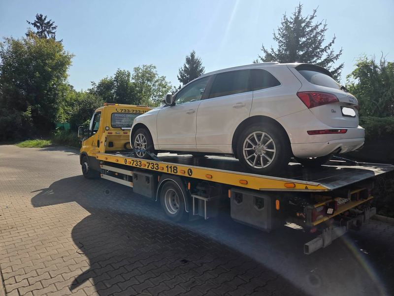 SUV transportowany lawetą pomocy drogowej Tuszyn na słonecznym parkingu wśród drzew