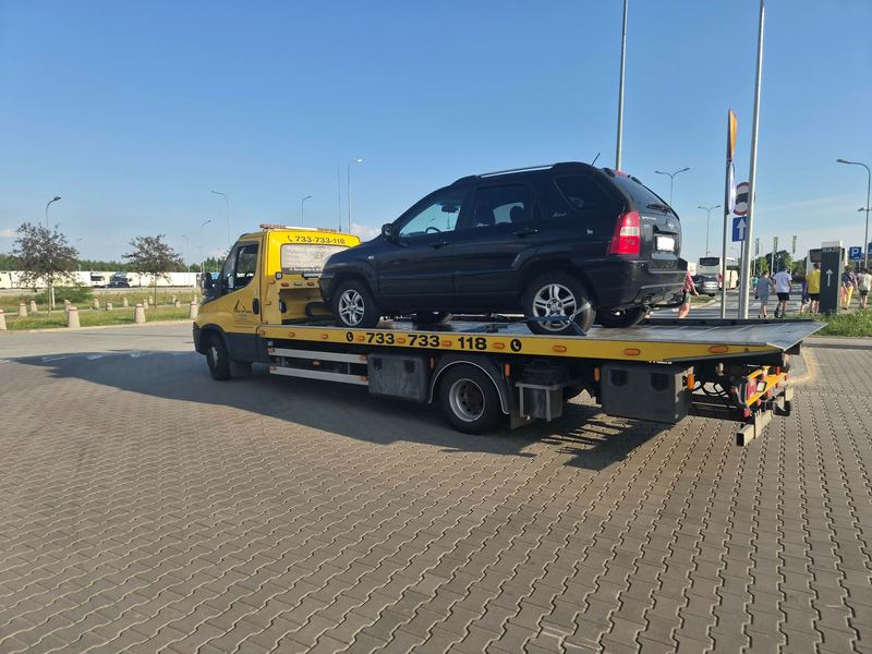 SUV zabezpieczony na lawecie pomocy drogowej Tuszyn stoi na tętniącym ruchem parkingu miejskim