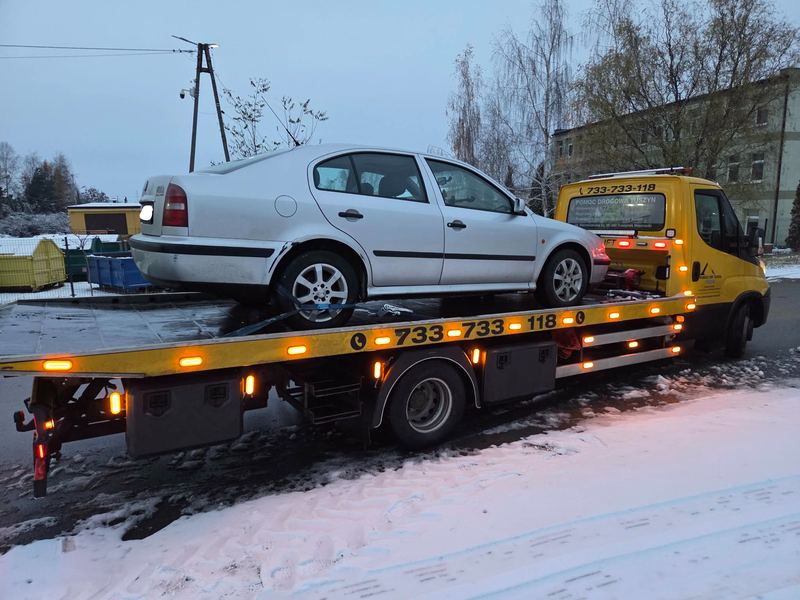 Sedan załadowany na lawetę pomocy drogowej Tuszyn stoi na ośnieżonej ulicy o zmierzchu